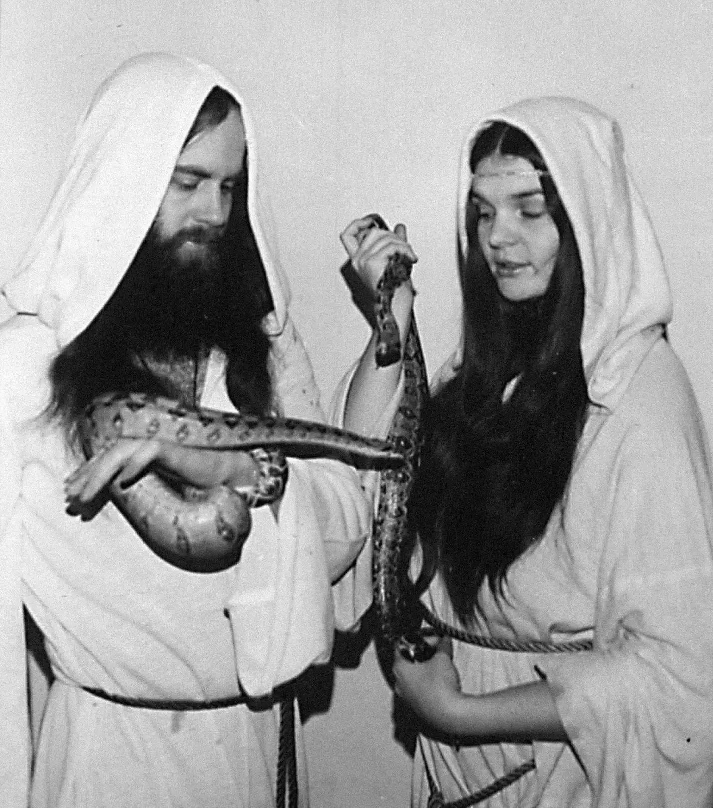 Oberon and Morning Glory, both wearing white cloaks, are standing together. Each is holding a large snake.